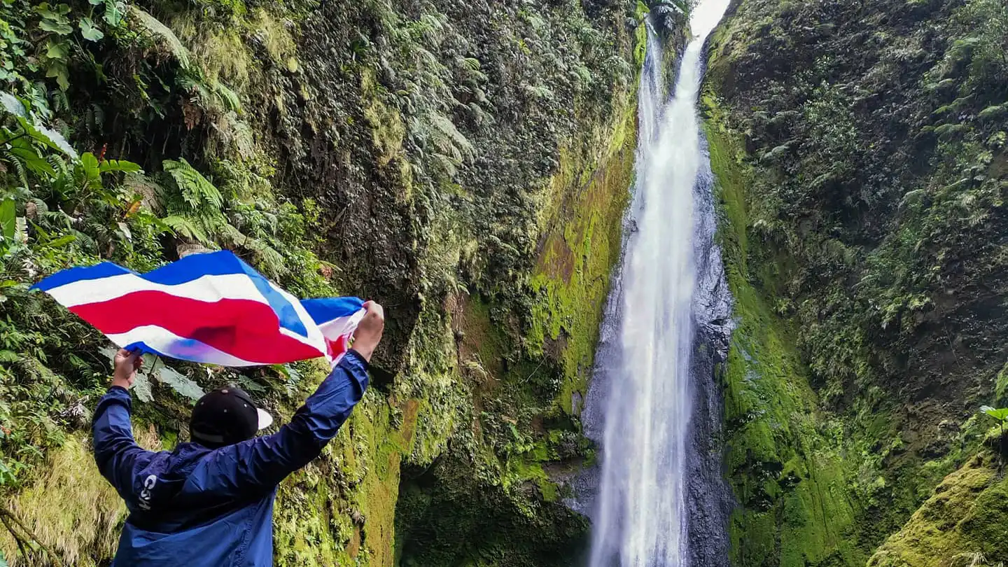A man holding a flag in front of a waterfall.
