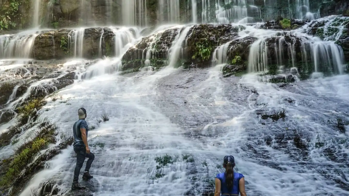 Duas pessoas em pé em frente a uma cachoeira