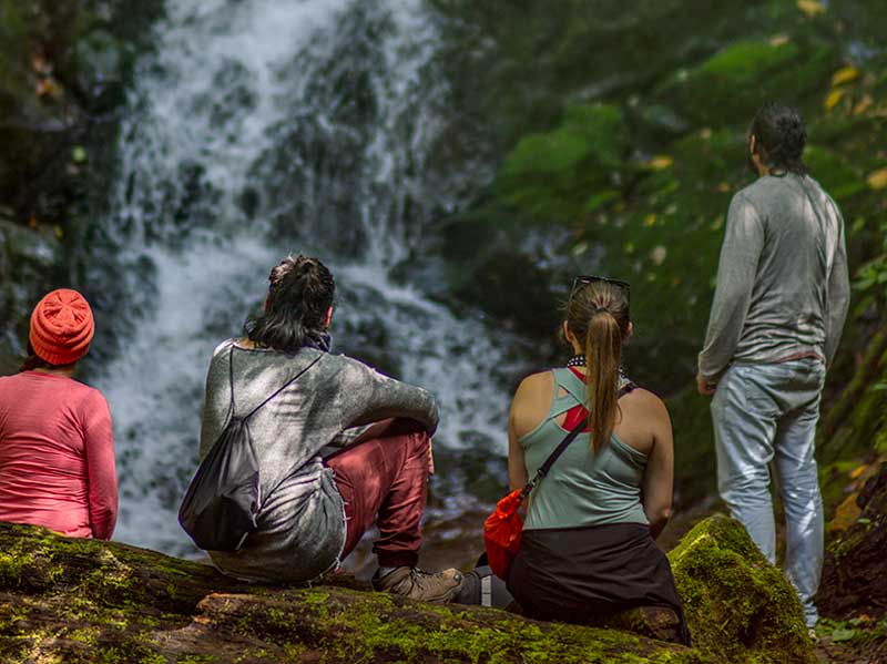A group of people sitting on a rock looking at a waterfall.