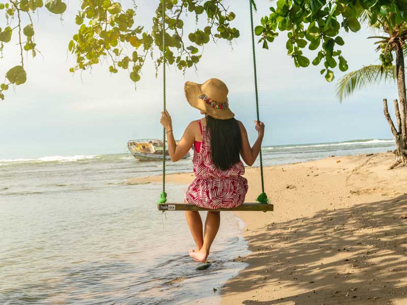 A woman sitting on a swing at the beach.