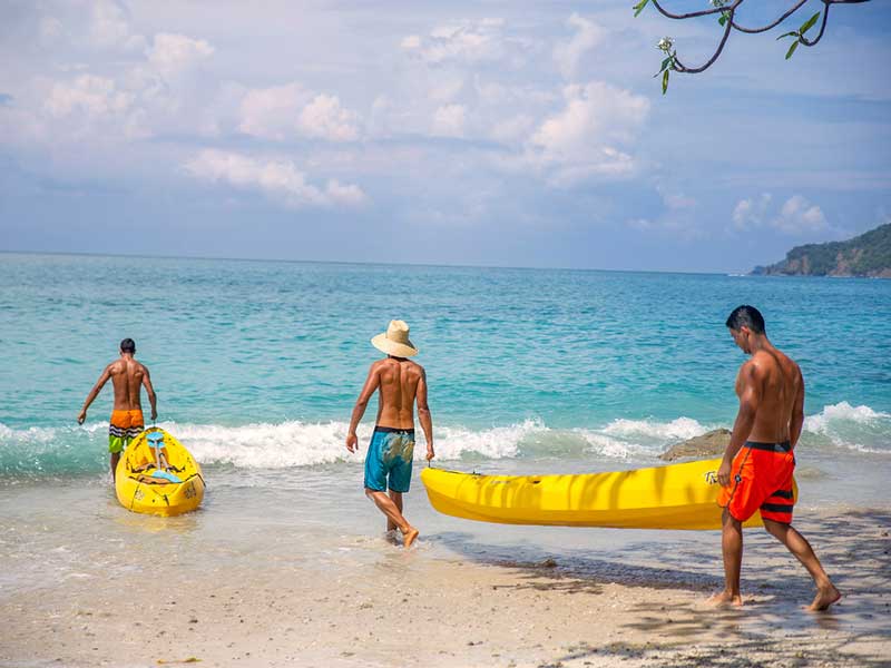 A group of people on a beach with a yellow surfboard.