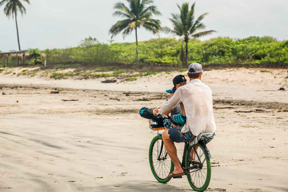 A man and a boy riding a bike on a beach.