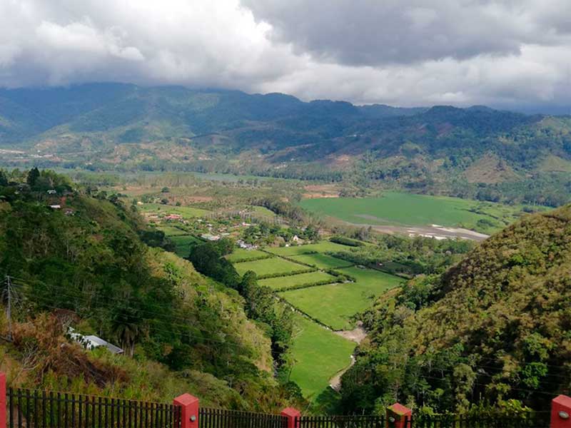 A lush green valley surrounded by mountains under a cloudy sky.