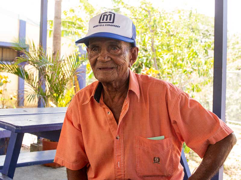 An old man wearing a hat sitting at a picnic table.