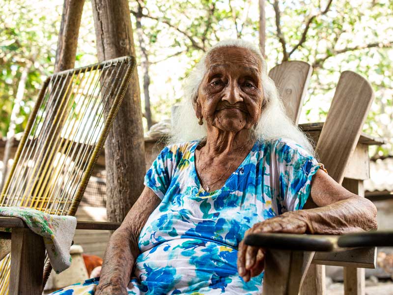 An old woman sitting in a chair outside.