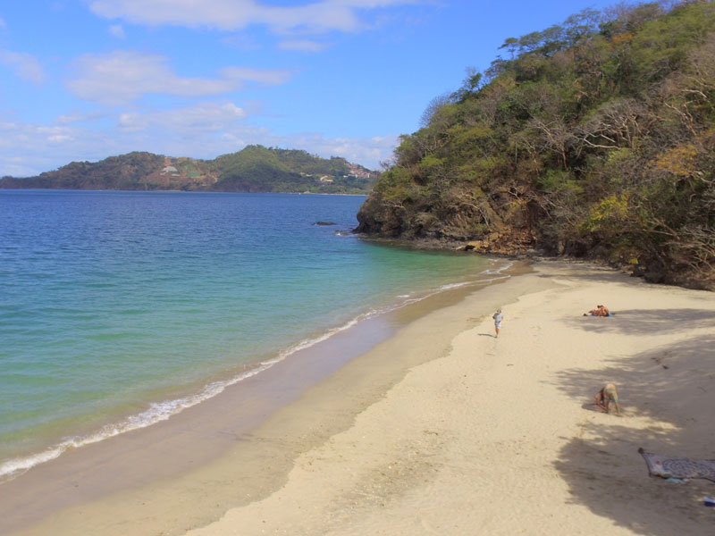 A sandy beach with a few people on it.