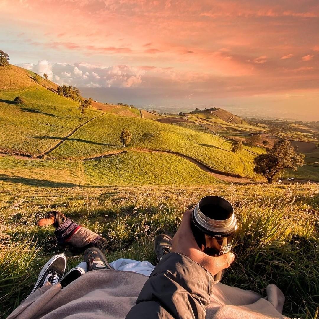 A man viewing a sunset at a lush green hillside