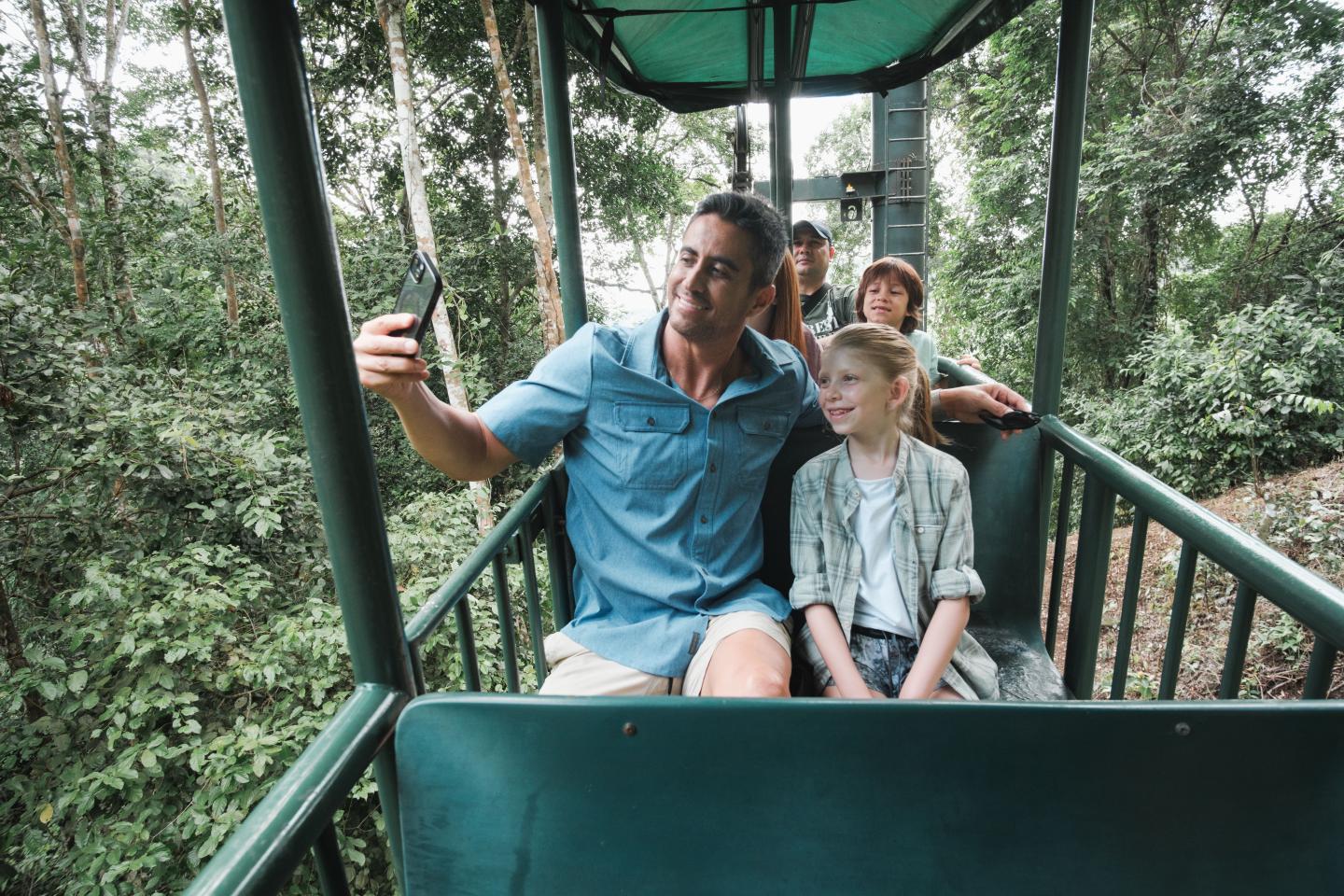 Family taking a selfie in an open-air gondola above the rainforest canopy.