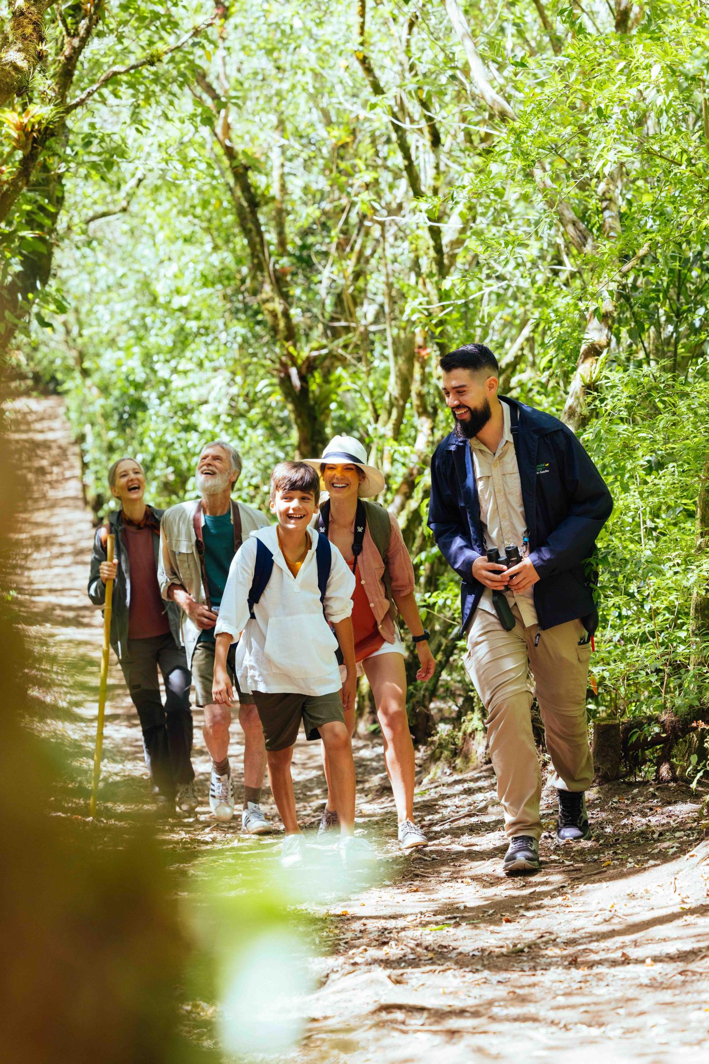 Small group of travelers walks along a shaded forest trail with a guide.